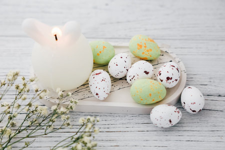 Decorative white candle bunny with speckled eggs on a wooden surface for Easter celebrationの写真素材