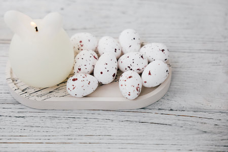 Decorative white candle bunny with speckled eggs on a wooden surface for Easter celebrationの写真素材