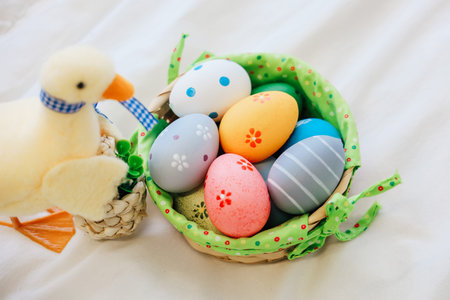 A vibrant basket filled with decorated Easter eggs sits next to a charming duck ornament on a soft...