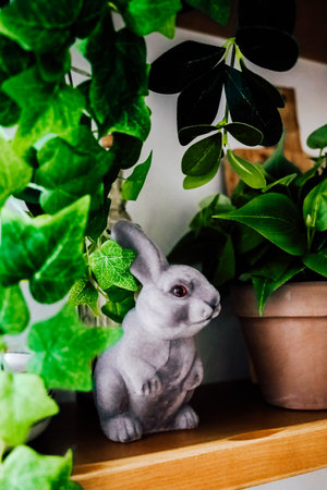 A charming bunny statue is nestled among vibrant green plants on a wooden shelf, creating a serene atmosphere.の写真素材