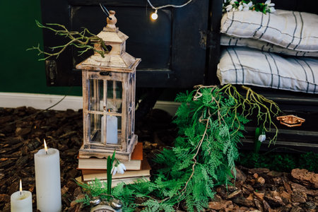 A lantern stands next to stacked books and candles, surrounded by greenery and decorative elements, creating a cozy atmosphere.の写真素材
