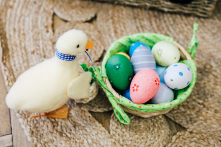 A fluffy chick stands next to a basket filled with vibrant Easter eggs, showcasing festive colors and designs during a spring holiday setup.の写真素材