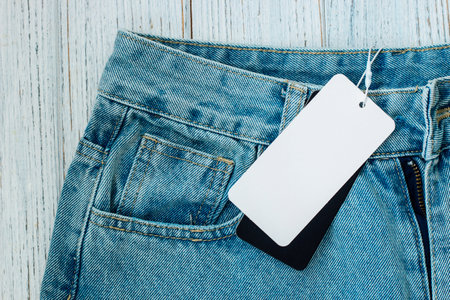 Denim jeans with a price tag lie on a rustic wooden surface, highlighting their casual style and affordability.の写真素材