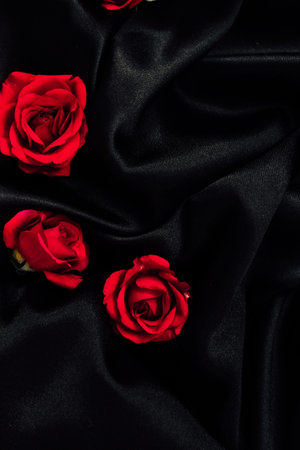 Red roses scattered on elegant black fabric creating a striking visual contrastの写真素材