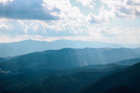 Golden rays pierce through clouds illuminating the rugged mountain range during the serene dusk enhancing the tranquil scenery.の写真素材