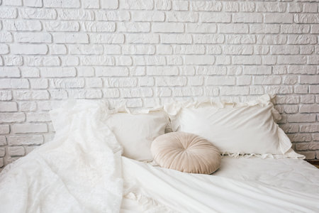 A cozy bedding arrangement features white pillows and a plush cushion against a white brick wall during daylight.の写真素材