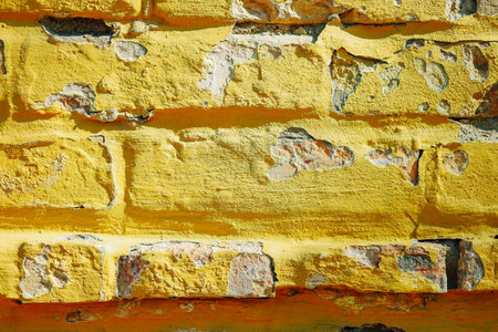 The surface features a bright yellow brick wall with significant peeling paint revealing its aged texture and unique character under sunlight.の写真素材