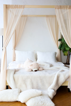 A serene bedroom features a four-poster bed draped with light fabric surrounded by cozy textiles and a plush teddy bear.の写真素材