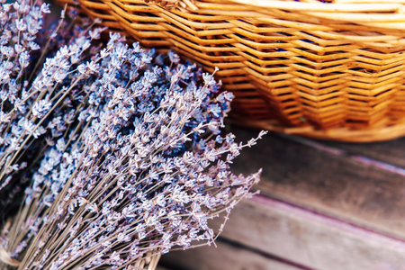 Dried lavender bundles are neatly arranged by a wicker basket on a wooden surface in a cozy environment.の写真素材