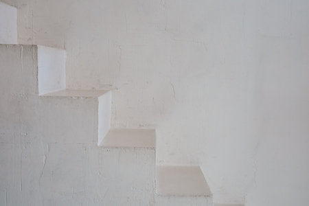 Striking white staircase with sharp angles leading up against a textured light wall in a modern interior environment.の写真素材