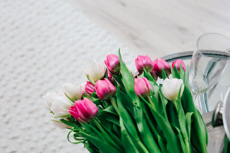 Colorful bouquet of pink and white tulips arranged elegantly on a round table with a glass vase in a...