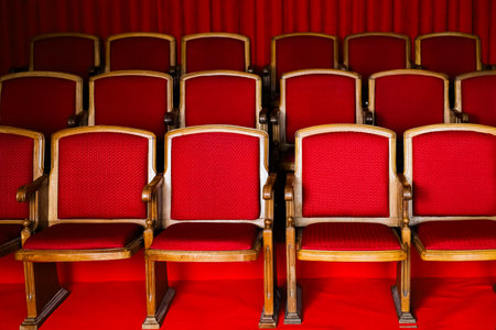 Empty red velvet chairs line up in neat rows against a matching luxurious curtain backdrop creating a classic theater atmosphere.の写真素材