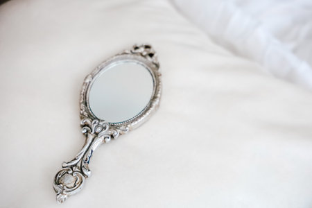 A vintage hand mirror rests on luxurious, white fabric, creating an elegant and serene atmosphere, perfect for a delicate aesthetic.の写真素材