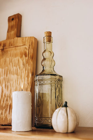 A rustic kitchen shelf displays a glass bottle with a cork a lit candle and a small decorative pumpkin showcasing autumn aesthetics.の写真素材
