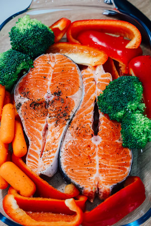Colorful salmon steaks are arranged with broccoli bell peppers and carrots in a baking dish poised...