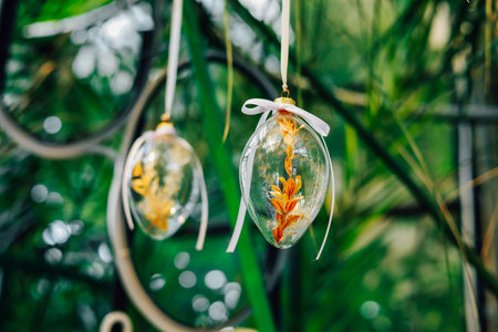 Delicate glass ornaments containing vibrant dried flowers are suspended amidst green foliage in a...