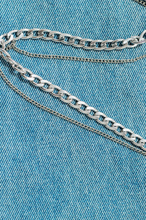 Close up view of intertwined silver chains resting on light blue denim fabric under natural...
