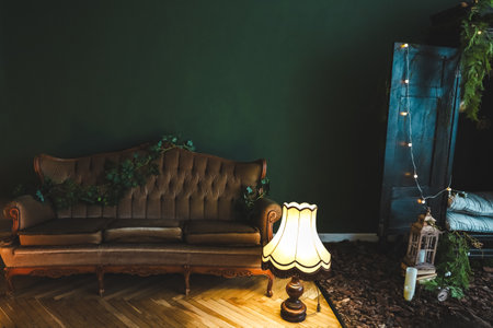 A stylish living space showcases a vintage sofa adorned with plants, a warm lamp, and gentle lighting, creating an inviting atmosphere.の写真素材