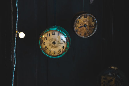 Two vintage clocks with patina hang on a dark wall, capturing the essence of timeless elegance in an antique space.の写真素材