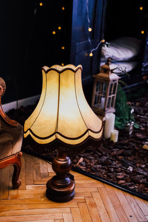 A vintage lamp with a soft glow stands next to a comfortable chair, adding warmth to a stylish indoor setting filled with plants and candles.の写真素材