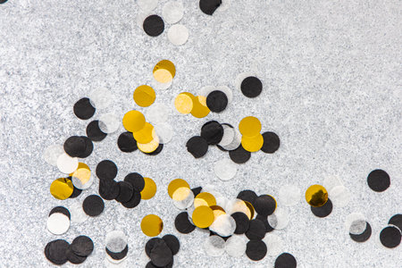 A variety of round confetti in black gold and white is strewn across a metallic silver surface adding a fun touch to the celebration.の写真素材