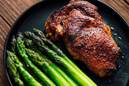 Juicy grilled steak rests beside vibrant green asparagus on a black plate showcasing a mouthwatering meal perfect for dinner.の写真素材