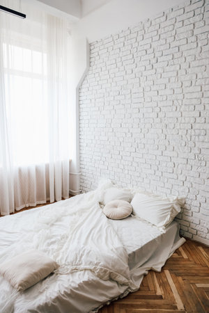Sunlight streams through sheer curtains into a cozy bedroom featuring a white brick wall and soft...