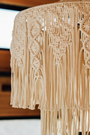 Beautiful macrame lamp shade features detailed knot work and fringe enhancing cozy ambiance in a modern living space.の写真素材