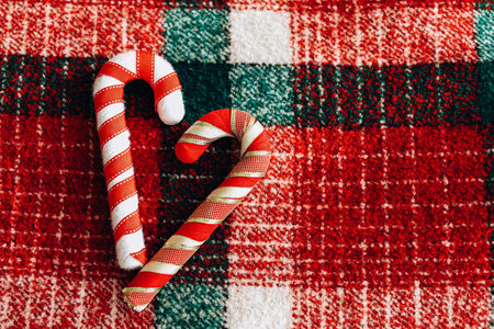 Two candy canes are placed in a heart shape on a cozy red and green plaid fabric enhancing the festive atmosphere during the holiday season.の写真素材