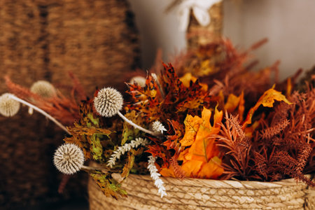 Colorful autumn leaves in shades of orange and yellow are artfully arranged with dried flowers in a...