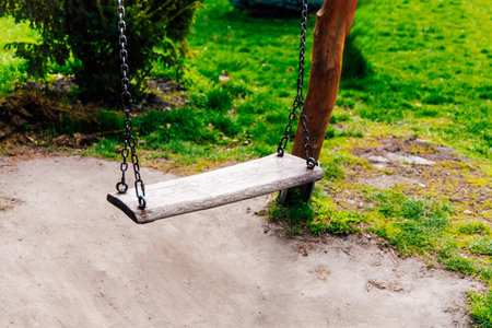 A solitary swing made of wood hangs from a sturdy tree in a vibrant park setting filled with lush green grass and foliage.の写真素材
