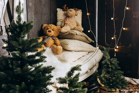 A snug Christmas corner features plush teddy bears resting on soft cushions surrounded by small Christmas trees and warm lights.の写真素材