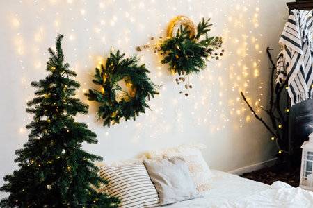 A comfortable room features a small tree and Christmas arranged wreaths on the wall illuminated by warm lights.の写真素材