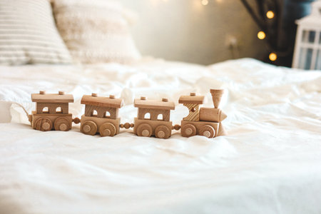 A charming wooden train toy set is arranged on a bed covered with soft blankets illuminated by gentle daylight creating a cozy atmosphere.の写真素材