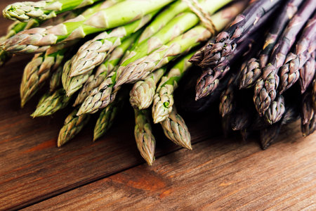 Fresh green and purple asparagus is arranged neatly on a rustic wooden table in a warm kitchen atmosphere ideal for cooking.の写真素材