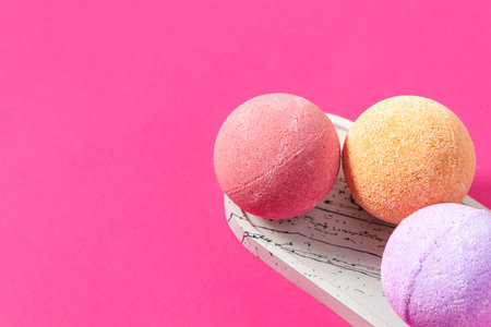 Three vibrant bath bombs in shades of pink orange and purple are displayed on a marble tray with a vivid pink backdrop.の写真素材
