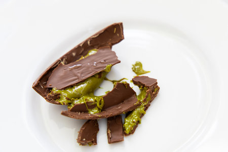 A piece of Dubai pistachio chocolate with a green filling splintered on a white plate showcasing a sweet unique dessert.の写真素材