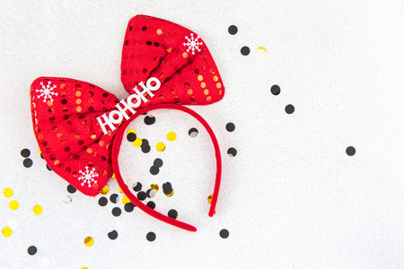 A bright red bow headband adorned with snowflakes and festive dots rests on a sparkling surface scattered with confetti.の写真素材