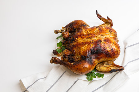 Golden brown roast chicken is arranged beautifully on a plate garnished with fresh herbs. A striped towel lies underneath adding a rustic touch.の写真素材