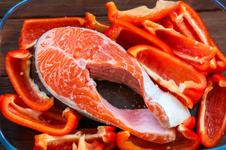 A fresh salmon steak is surrounded by vibrant red bell pepper slices ready for cooking.の写真素材