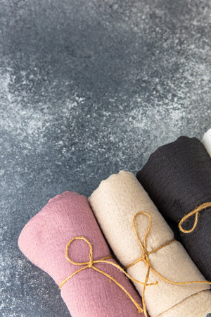 Four rolls of fabric in different colors are tied with twine resting on a rustic gray backdrop ideal for crafting projects.の写真素材
