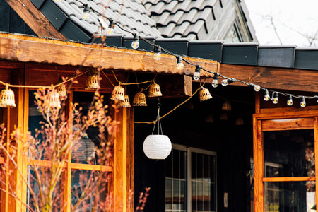 String lights and lanterns adorn the rustic exterior of a charming cottage during daylight...