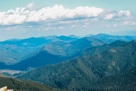 A breathtaking panorama reveals rolling mountain ranges covered in dense forests under a clear blue...