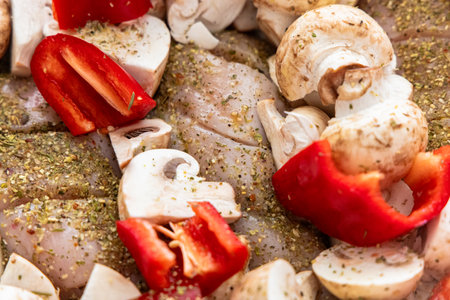 Marinated chicken pieces are seasoned and mixed with sliced red bell peppers and mushrooms before grilling.の写真素材