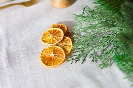 Dried orange slices are placed on a linen tablecloth accompanied by green foliage creating a natural decorative display.の写真素材