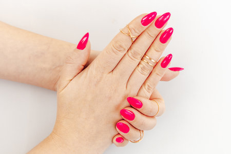 Close-up of hands displaying vibrant long pink nails elegantly complemented by multiple gold rings against a light background.の写真素材