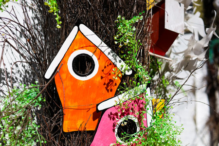 Two painted birdhouses in orange and pink hang on a tree surrounded by greenery creating a lively garden setting.の写真素材