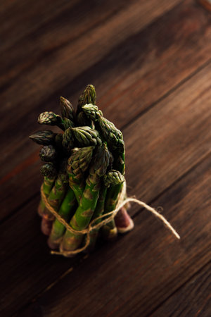 A bundle of green asparagus is neatly tied with twine resting on a rustic wooden table. Soft natural light enhances its vibrant color.の写真素材