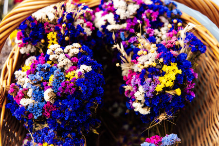 A wicker basket filled with vibrant dried flowers showcasing shades of purple blue and yellow rests at a bustling market in the afternoon light.の写真素材