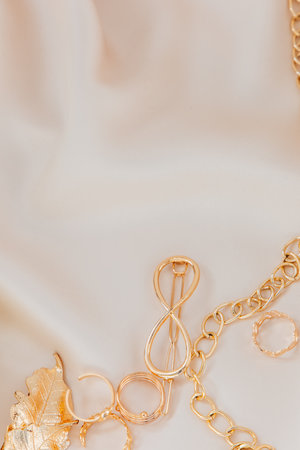 Various pieces of golden jewelry are artistically displayed on a smooth neutral-colored fabric showcasing their intricate designs.の写真素材